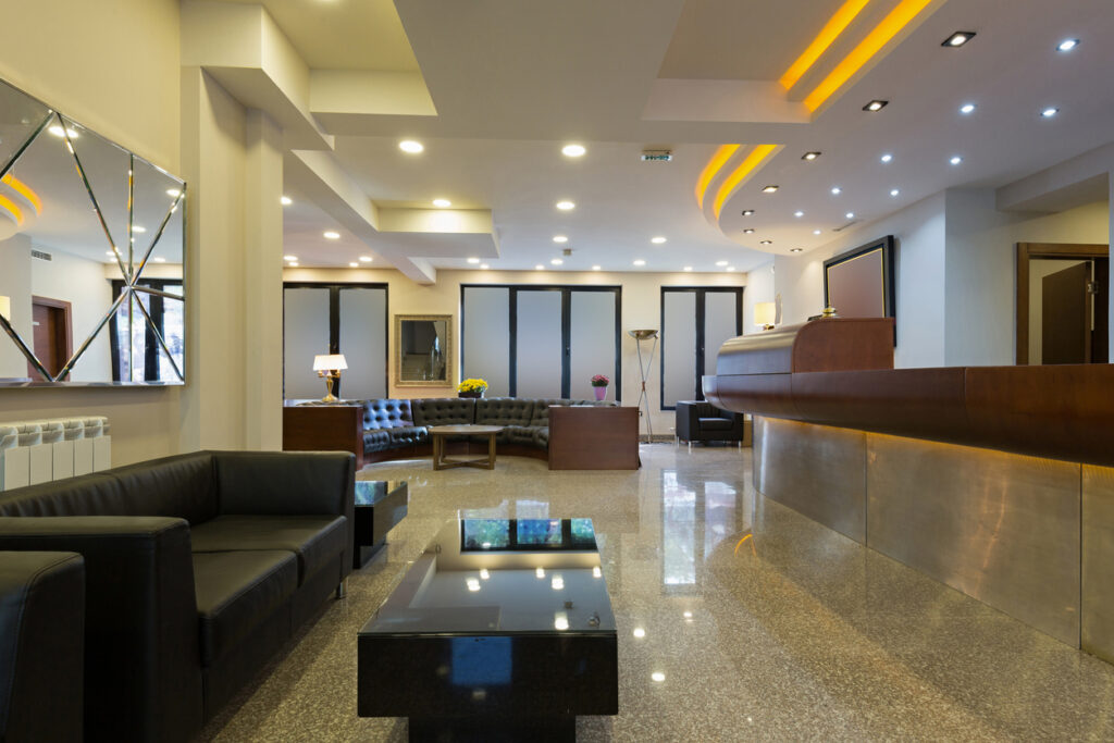 Contemporary hotel reception area with LED lighting, black leather furniture, and a wooden reception desk.